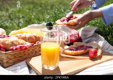Donna con croissant all'aperto, focalizzata su un bicchiere di succo. Picnic estivo Foto Stock