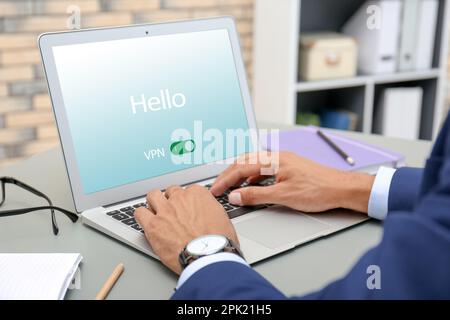 Uomo che utilizza un laptop con VPN attivata al tavolo, primo piano Foto Stock