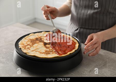 Donna che cucina deliziosa crepe con marmellata su elettrico frittella in cucina, primo piano Foto Stock