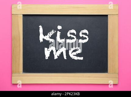 Piccola lavagna con frase Kiss Me su sfondo rosa, vista dall'alto Foto Stock