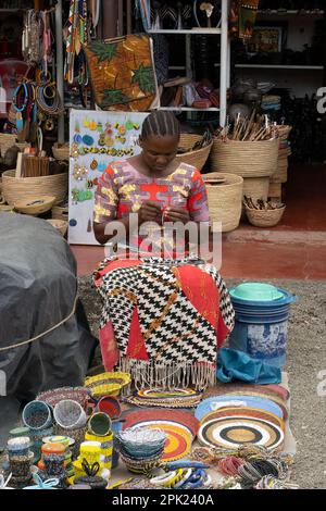 Arusha, Tanzania - 17th ottobre 2022: Una donna che fa e vende prodotti a perline colorate nel mercato di Arusha, Tanzania. Foto Stock