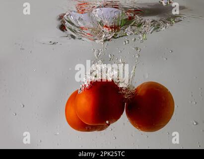 Pomodoro maturo cade profondamente sotto l'acqua con un grande splash. Foto Stock