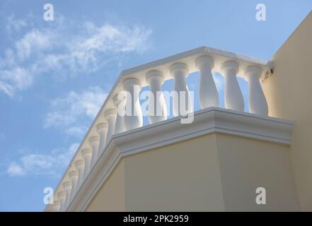 Primo piano balaustra bianca in cemento sopra pareti intonacate e dipinte gialle su cielo blu. Foto Stock