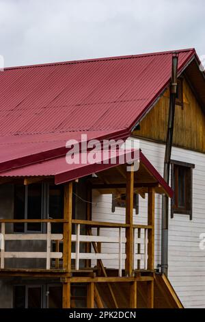 Casa con tetto in tegole di metallo marrone e grondaia. Grondaia metallica sistema, grondaia e tubo di drenaggio esterno. Foto Stock