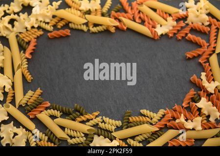 Primo piano dall'alto di una tavola di ardesia con diversi tipi di pasta italiana come penne, mafalda corta e fusilli.sfondo scuro, spac copia Foto Stock