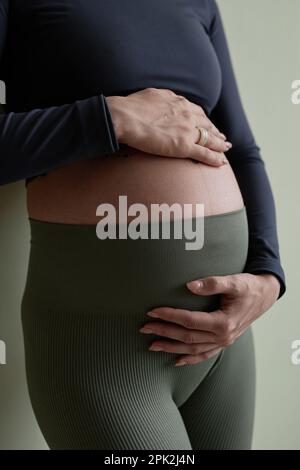 Primo piano verticale di una donna sportiva incinta che indossa abbigliamento sportivo e tiene la pancia Foto Stock