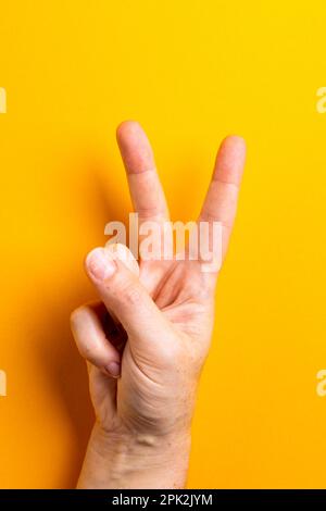 Primo piano di mano della donna caucasica che mostra un segno di pace con spazio copia su sfondo giallo Foto Stock