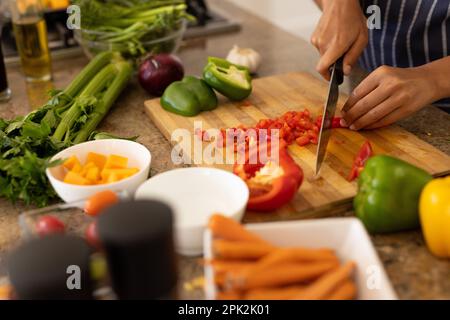 Mani tagliate di giovane donna biraciale che taglia i pomodori sul tagliere in cucina Foto Stock