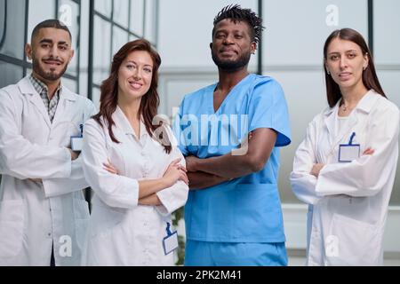 Un gruppo multietnico di quattro medici e infermieri che si trovano in un corridoio ospedaliero e indossano abiti e abiti. Foto Stock