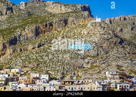 Cappella bianca e bandiera greca dipinta sulla collina sopra Pothia, la città principale di Kalymnos, isola greca, Isole Dodecanesi, Grecia Foto Stock