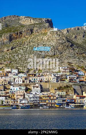 Cappella bianca e bandiera greca dipinta sulla collina sopra Pothia, la città principale di Kalymnos, isola greca, Isole Dodecanesi, Grecia Foto Stock