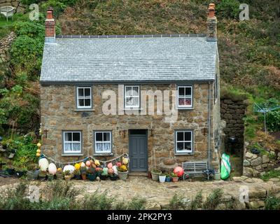 Bella vecchia pietra di granito Cornish cottage sul mare con tetto in ardesia e galleggianti da pesca e boe a Penberth Cove, Cornwall, Regno Unito Foto Stock