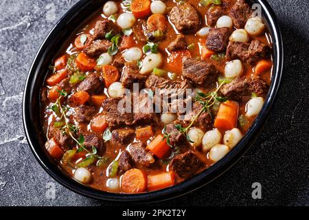 costolette di manzo disossate stufati con carote e cipolle in ciotola nera su tavolo di cemento, primo piano Foto Stock