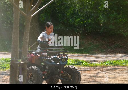 Bambina asiatica a 9 anni per la prima volta in moto ATV da sola, in pista sotto la luce del sole, attività all'aperto Foto Stock