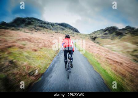 Ciclista maschio su strada fino a Hardknott Pass, Eskdale, Cumbria, Regno Unito. Foto Stock