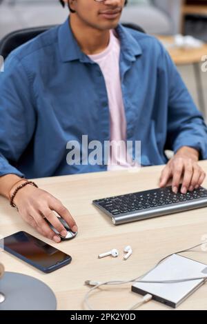 Ripresa verticale ritagliata di un giovane uomo nero utilizzando il computer con messa a fuoco sul mouse mano maschile Foto Stock