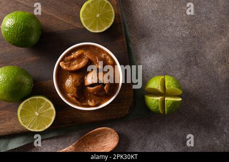 Pickle di lime dello Sri Lanka fatto in casa di lime, sale, peperoncino, pepe su fondo marrone. Vista dall'alto. Spazio di copia. Foto Stock