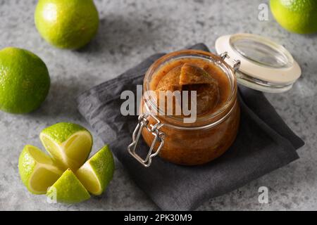 Tradizionale cime di lime dello Sri Lanka, sale, peperoncino, pepe in vasetto di conserva di vetro su fondo grigio. Primo piano. Foto Stock