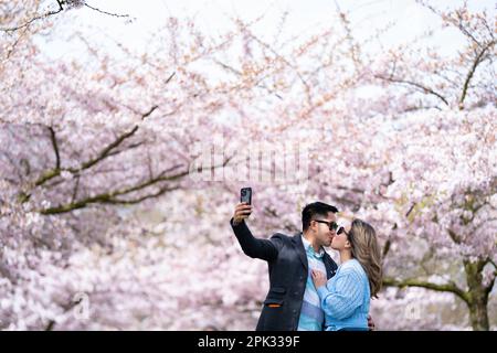 Una coppia prende un selfie con alberi di ciliegio a Battersea Park nel sud-ovest di Londra. Data immagine: Mercoledì 5 aprile 2023. Foto Stock