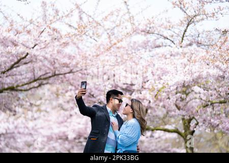 Una coppia prende un selfie con alberi di ciliegio a Battersea Park nel sud-ovest di Londra. Data immagine: Mercoledì 5 aprile 2023. Foto Stock