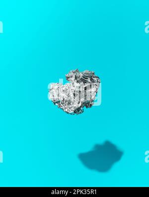 Sfera di lamina di alluminio sgualcita galleggiante a mezz'aria su sfondo blu Foto Stock