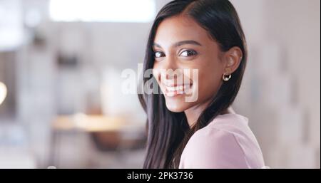 Donna d'affari alla moda che guarda felice e sorridente mentre si siede nel suo ufficio. Professionista creativo con un atteggiamento positivo e una sensazione mentale Foto Stock