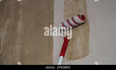 primo piano di un rullo a righe rosse e bianche per l'applicazione di colla, stucco o primer sulla superficie della parete, lo strumento di lavoro del pittore nel processo Foto Stock