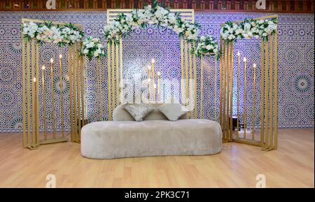 Un matrimonio in stile tradizionale marocchino allestito elegantemente con un grande divano per la coppia di nozze da sedere e ricevere benedizioni dagli ospiti, circondato Foto Stock