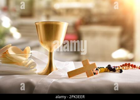 Calice con vino e ostie consacrate in un contenitore su tavola con croce cristiana sull'altare. Vista frontale. Foto Stock