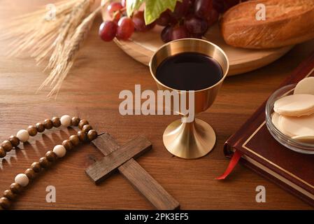 Bicchiere di vino e ostie consacrate su tavola di legno con croce cristiana bibbia ed elementi santi. Vista rialzata. Foto Stock