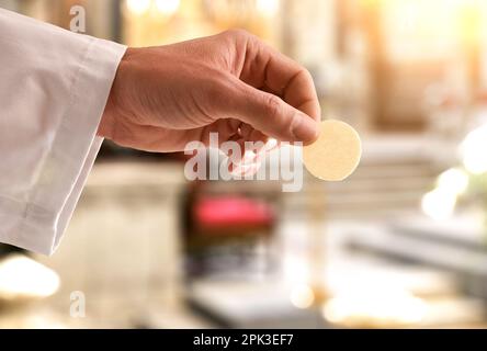 Particolare della mano di un sacerdote che dà un'ostia consacrata per la comunione in una chiesa. Vista laterale. Foto Stock