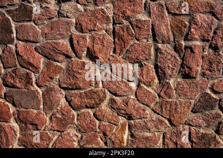 Un muro fatto di pietre naturali ruvide, rosse, tagliate. Può essere utilizzato come immagine di sfondo. Foto Stock