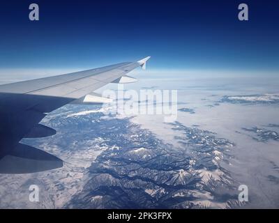 Volo in aereo sopra le vette innevate dei Carpazi. Skyline blu e ala dell'aeroplano visti attraverso la finestra Foto Stock