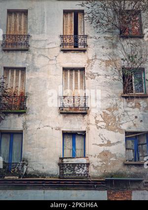 Facciata di un edificio abbandonato. Alberi e cespugli che crescono dalle finestre, feritoie arrugginite e pareti in cemento incrinato Foto Stock