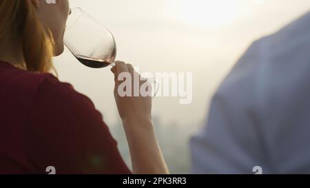 Donna in possesso di vino rosso bere vino con il tramonto sulla vista della città alto edificio Foto Stock