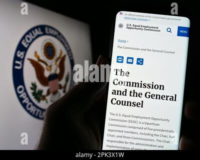 Persona che tiene il cellulare con pagina web della Commissione di pari opportunità di impiego (EOC) sullo schermo con il logo. Messa a fuoco al centro del display del telefono. Foto Stock