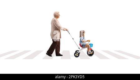 Immagine a tutto profilo di una nonna che spinge un bambino su un triciclo attraverso un passaggio pedonale isolato su sfondo bianco Foto Stock