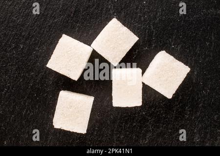 Diversi cubetti di zucchero bianco su pietra ardesia, macro, vista dall'alto. Foto Stock