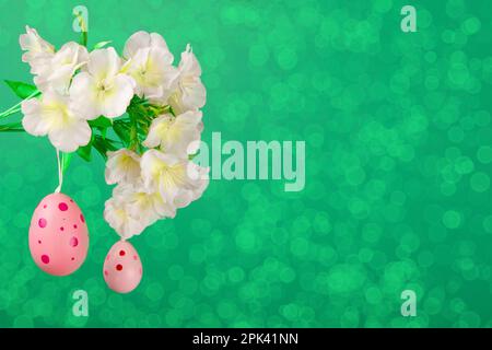 Due uova rosa di Pasqua appese da un ramo fiorito su uno sfondo verde lussureggiante Foto Stock