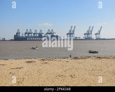 Vista dalla spiaggia di Harwich che guarda dall'estuario alle gru giganti nel porto di Felixstowe e una grande nave container 'Evergreen' nei moli. Foto Stock