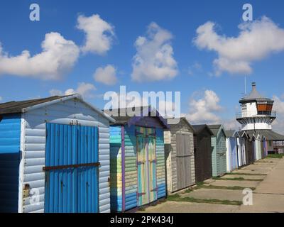 Harwich, una stazione balneare inglese: Vista iconica delle capanne sulla spiaggia dai colori vivaci sul lungomare con il Faro basso in lontananza. Foto Stock