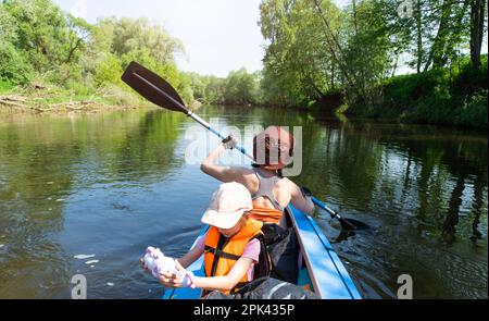 Gita in kayak in famiglia. Mamma e figlia canottano una barca sul fiume, un'escursione in acqua, un'avventura estiva. Eco-friendly e turismo estremo, attivo e sano Foto Stock