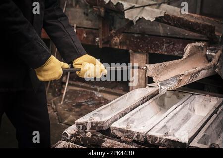 Lavoratore di fonderia che versa metallo liquido in stampi. Fusione di alluminio o argento Foto Stock