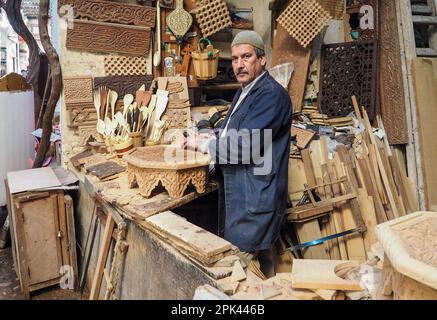 Fez, Marocco - 07 gennaio 2020: Uomo sconosciuto nella sua lavorazione del legno o scultura officina vicino al mercato di strada. molti souvenir di legno e prodotti intorno a lui Foto Stock