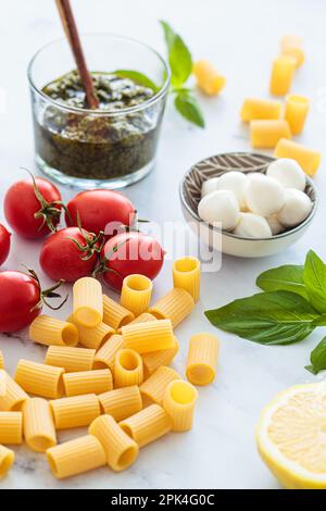 Ingredienti crudi per cucinare pasta vegetariana con pomodori, pesto e mozzarella. Concetto di cucina italiana. Foto Stock