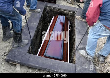 I lavoratori comunali sollevano le bare in tombe durante la cerimonia funeraria dei militari ucraini Foto Stock