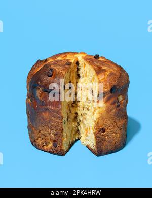 Panettone a fette in chiaro minimalista su un tavolo blu. Delizioso panettone di pasta madre fatto in casa con uvetta, scorza d'arancia candita e cioccolato Foto Stock