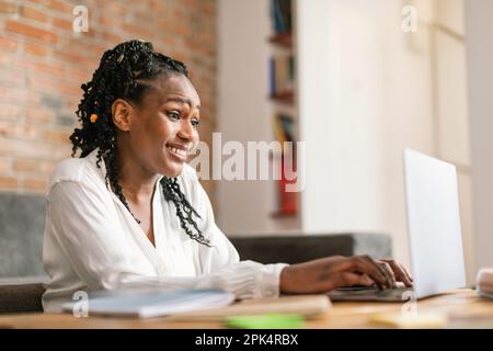 Donna afroamericana sorridente che scrive sul laptop, che lavora o studia online da casa, spazio libero Foto Stock