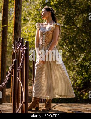 Giovane donna in un Cottage Core Attire su un ponte circondato da alberi | DOF | retroilluminazione | toni caldi Foto Stock