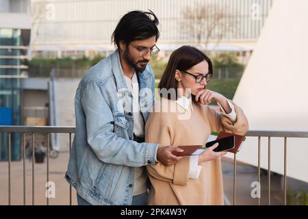 Triste e penoso giovane uomo e donna internazionale in casual e occhiali con passaporto e biglietti Foto Stock